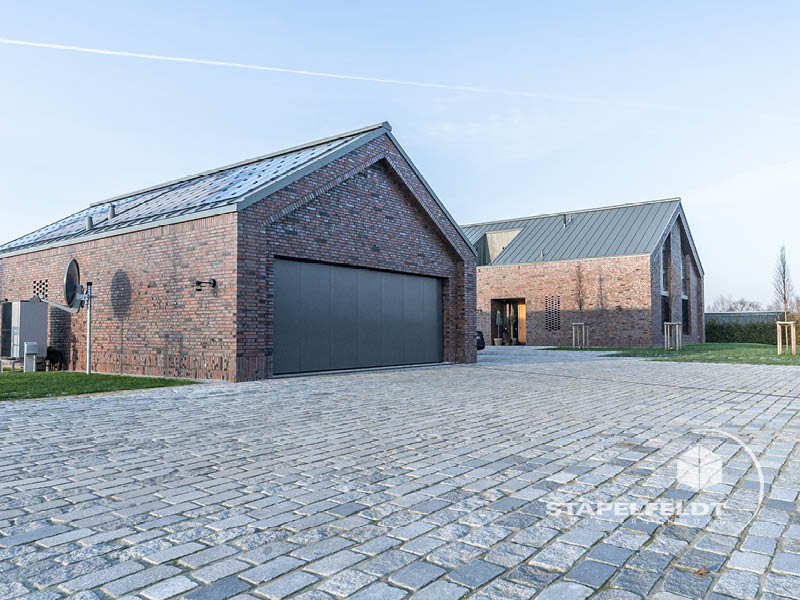 Nebengebäude mit großem Garagentor und gepflastertem Hof vor dem Klinkerneubau in Hamburg-Curslack