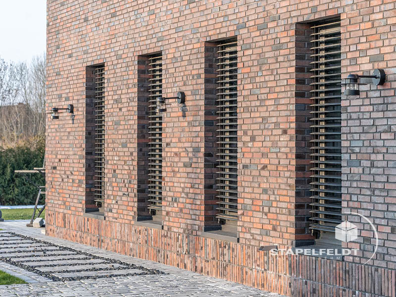 Klinkerfassade mit vertikalen Fensteröffnungen, außenliegenden Lamellen und Wandleuchten in Hamburg-Curslack