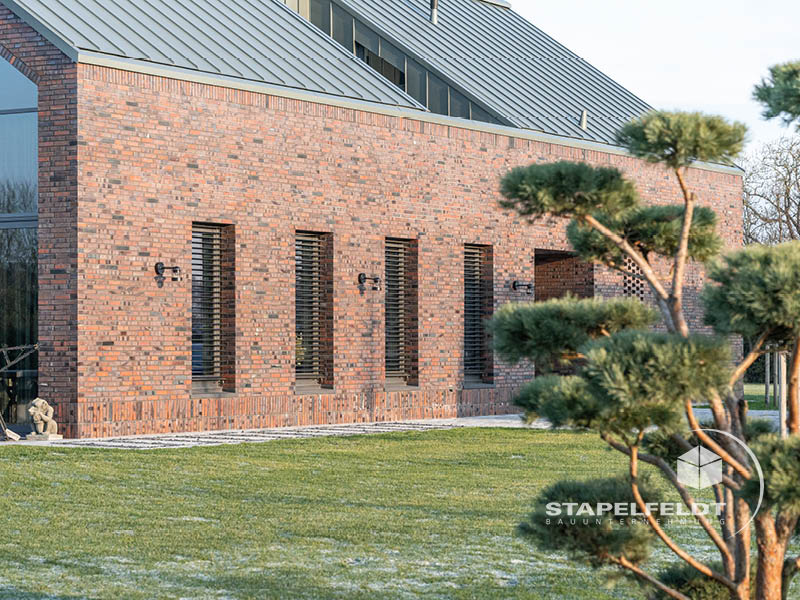 Längsfassade des Klinkerneubaus mit schmalen Fensteröffnungen und Metall­dach in Hamburg-Curslack