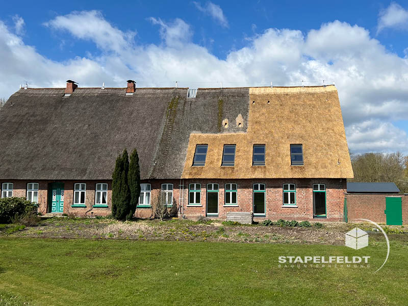 Historisches Reetdachhaus in Hamburg-Allermöhe mit teilweise umgebautem Mauerwerk, erneuertem Dach und grünen Türen.