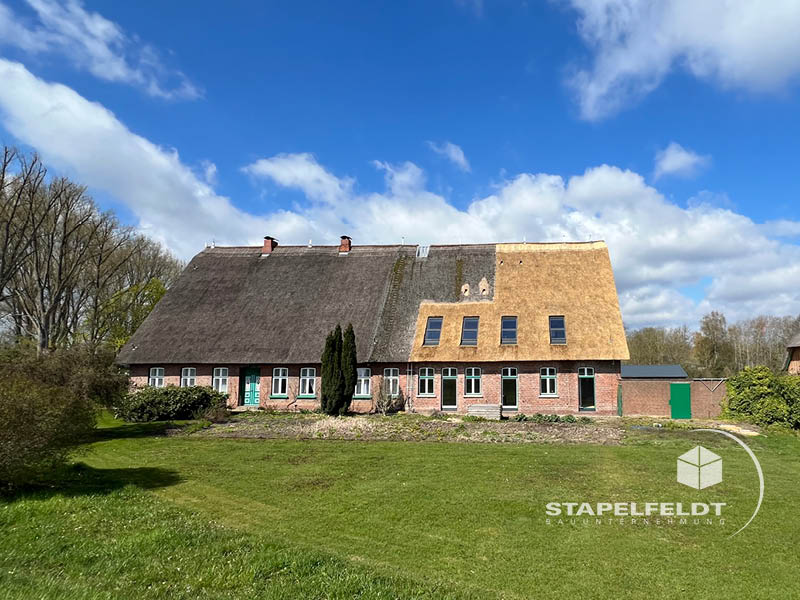 Weitwinkelaufnahme des historischen, umgebauten Reetdachhauses in Hamburg-Allermöhe mit Wiese und teilweise erneuertem Dach.